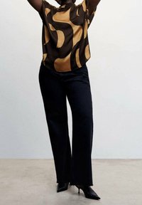 Blouse à manches courtes, coupe ample, avec un motif abstrait noir et or, associée  à un jean droit foncé et des escarpins noirs pointus.