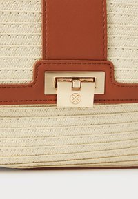 Hnědá kožená a smetanová tkaná kabelka s ozdobným zlatým zámkem, textura povrchu a charakteristický vzor stehu.