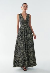 Vestido maxi negro con patrón de ondas crema, escote en V, cintura ajustada y falda fluida. Cuenta con botones decorativos en el centro y un diseño elegante.