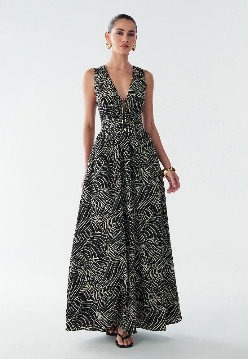 Vestido maxi negro con patrón de ondas crema, escote en V, cintura ajustada y falda fluida. Cuenta con botones decorativos en el centro y un diseño elegante.