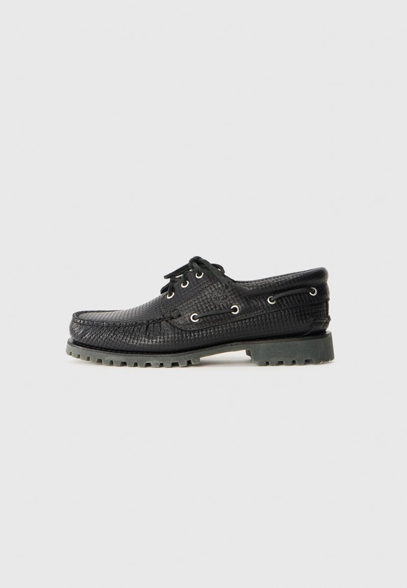 Chaussure noire en cuir texturé à lacets avec semelle épaisse à rainures, œillets métalliques et couture style mocassin sur un fond clair uni.
