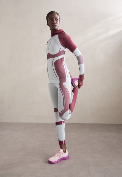 Szorosan illeszkedő sportöltözet fehér alapszínen bordó díszítéssel; bordázott anyag; kapucnis felső és teljes hosszúságú leggings; világos rózsaszín sportcipők lila talppal.