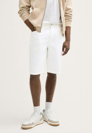 Białe szorty o dopasowanym kroju, z gładką fakturą, bocznymi kieszeniami i prostym wykończeniem. Zestawione z białymi trampkami i skarpetkami.