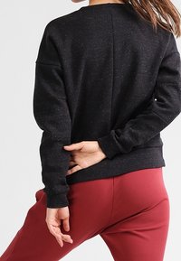 Sweat-shirt noir à finition texturée, épaules tombantes et encolure ronde, associé à un pantalon rouge. Présente une couture au dos et une coupe décontractée.