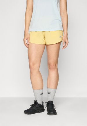 Light yellow athletic shorts with side cut edges, paired with gray crew socks and black running shoes. Simple design, no visible patterns.