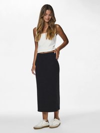 Μαύρη μίντι φούστα με ρίγες και λευκό κοντό τοπ, συνδυασμένα με λευκά αθλητικά παπούτσια. Η φούστα έχει εφαρμοστή γραμμή και φτάνει μέχρι τη μέση της γάμπας.