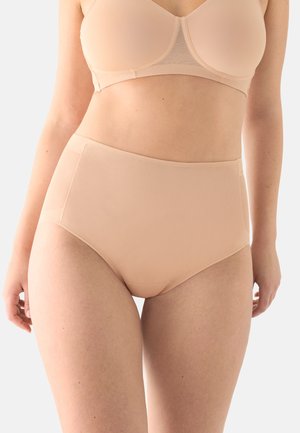 Mujer con ropa interior de talle alto color nude y sujetador a juego, sobre un fondo claro y liso.