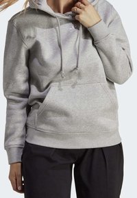 Grå huva sweatshirt gjord av mjukt tyg, med en framficka, dragsnoddar och ribbade ärmslut, visas med svarta byxor.