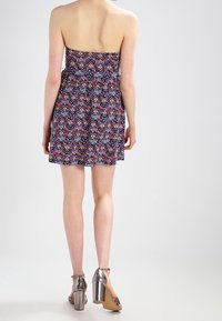 Robe sans bretelles avec un motif géométrique en marine, rose et blanc ; corsage ajusté, jupe évasée et tissu léger. Talons blocs argentés.