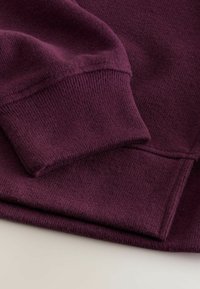 Tissu de sweatshirt violet avec une surface texturée. Les poignets et l'ourlet présentent des détails côtes. Apparence générale douce, avec une coupe décontractée.