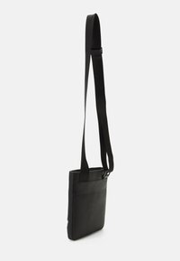 Borsa a tracolla nera realizzata in materiale texturizzato con forma piatta. Dotata di una lunga tracolla regolabile e un design semplice e pulito.