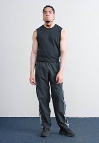 Top sportiv negru fără mâneci și pantaloni negri asortați cu dungi albe pe laterale. Îmbrăcămintea este fabricată dintr-un material neted și ușor.