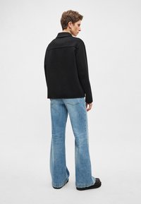 Casaco preto de mistura de lã com gola, combinado com jeans azul claro de cintura alta e flare e botas plataforma pretas, visto de costas.