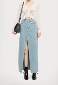 Jasnoniebieska maxi spódnica z denimu z przednim rozcięciem. Połączona z kremowym, dzianinowym kardiganem i czarnymi botkami za kostkę. Dodatki obejmują czarną torbę.