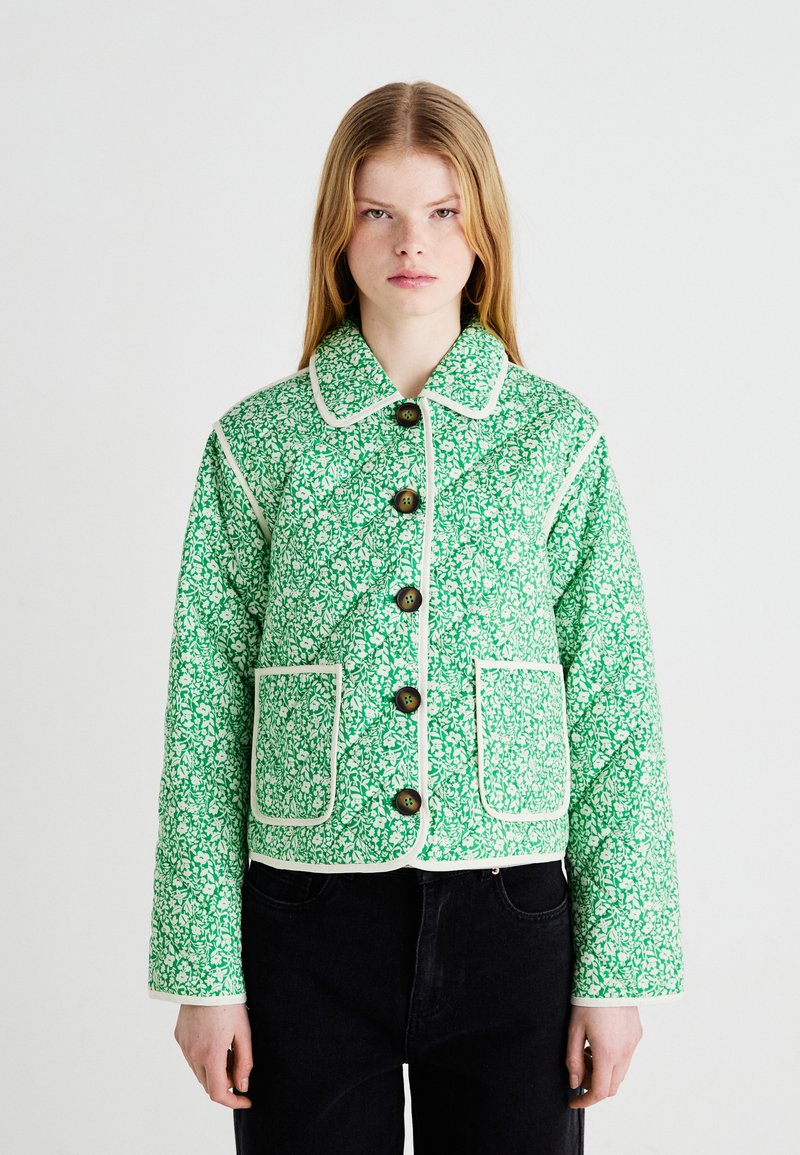 Giacca trapuntata floreale verde con piping bianco, dotata di colletto, bottoni frontali e due tasche a patta. Motivo testurizzato su tutta la superficie.