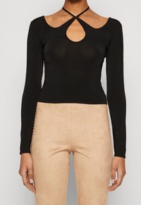 Top nero a maniche lunghe con design aderente, caratterizzato da un'apertura a forma di chiave nel colletto e spalline incrociate. Tessuto morbido, abbinato a pantaloni in suede color cammello.