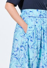 Una gonna a fantasia floreale blu con una vita arricciata, dotata di tasche laterali e realizzata in un tessuto leggero con una texture morbida.