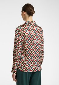 Blusa a maniche lunghe con un motivo geometrico in rosso, blu e beige, realizzata in tessuto leggero, con colletto e polsini con bottoni.