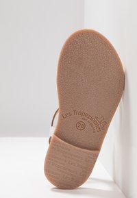 Suela de goma marrón con superficie texturizada y nombre de la marca en relieve. Correas de cuero blanco que se sujetan en el talón y el arco, con la talla 28 indicada.