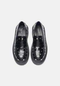 Mocassins en cuir noir avec des accents en clous argentés, design à bout rond et semelles en caoutchouc épaisses. Texture lisse avec des détails de couture décorative.
