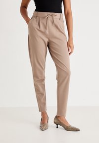 Beige tailored broek met een tailleband van trekkoord, zijzakken en een aansluitende pasvorm, gecombineerd met metallic puntige hakken.