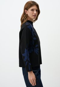 Zwarte trui met een hoge hals en lange mouwen, versierd met een donkerblauw bloemenpatroon dat vanaf de schouder doorloopt.