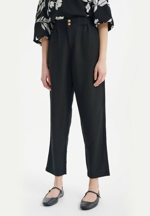 Pantaloni neri a gamba larga con una vestibilità comoda, dotati di una fascia elastica in vita e due bottoni, realizzati in un tessuto leggero, abbinati a delle ballerine nere.