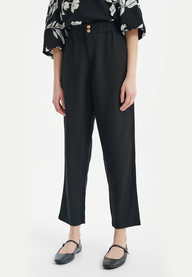 Zwarte wijde broek met een relaxte pasvorm, voorzien van een elastische tailleband en twee knopen, gemaakt van lichtgewicht stof, gecombineerd met zwarte ballerina's.