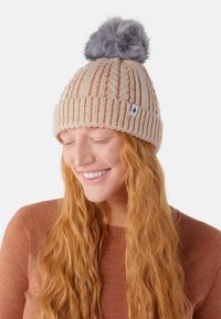Cappello lavorato a maglia color beige chiaro con un design a coste testurizzato e un pompon in pelliccia sintetica grigia sulla parte superiore. Presenta un piccolo patch con logo sul lato.