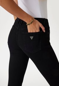 Jeans skinny negros de cintura alta, con un parche de logo triangular en el bolsillo trasero y una textura de denim suave.