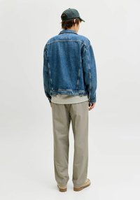 Veste en jean coupe décontractée, couleur bleu clair avec coutures visibles. Associée à un pantalon large beige et une chemise rayée en dessous.