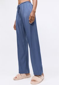Lichte blauwe broek met een elastische tailleband en trekkoord. Glad materiaal met een ontspannen pasvorm, gecombineerd met fluffy beige pantoffels.