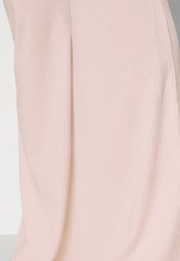 Tecido em rosa claro com textura canelada e um brilho subtil. O design apresenta caimento suave e é ligeiramente translúcido em algumas áreas.
