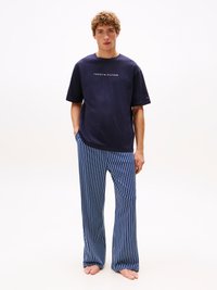 Jūras spēku īsām piedurknēm t-krekls ar "TOMMY HILFIGER" logo, apvienots ar zilo un balto vertikāli svītroto mājas biksēm, abas izgatavotas no mīkstas auduma.