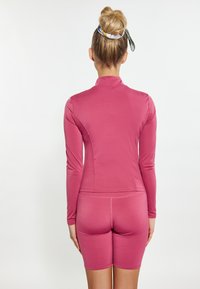 Outfit sportivo aderente di colore rosa solido, con maniche lunghe e design con collo alto. Il materiale sembra liscio ed elastico.