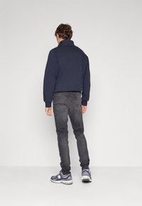 Marinblå kort sweatshirt, grå skinny jeans och blå sneakers med vita detaljer. Slät tyg, minimalistisk design och figurnära silhuett.