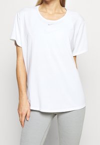 Camiseta blanca de manga corta hecha de tejido de algodón, con cuello redondo y un pequeño logo gris de Nike en el pecho.