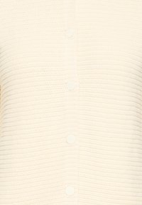 Gros plan sur un cardigan tricoté de couleur crème avec une rangée verticale de cinq boutons ronds au centre.