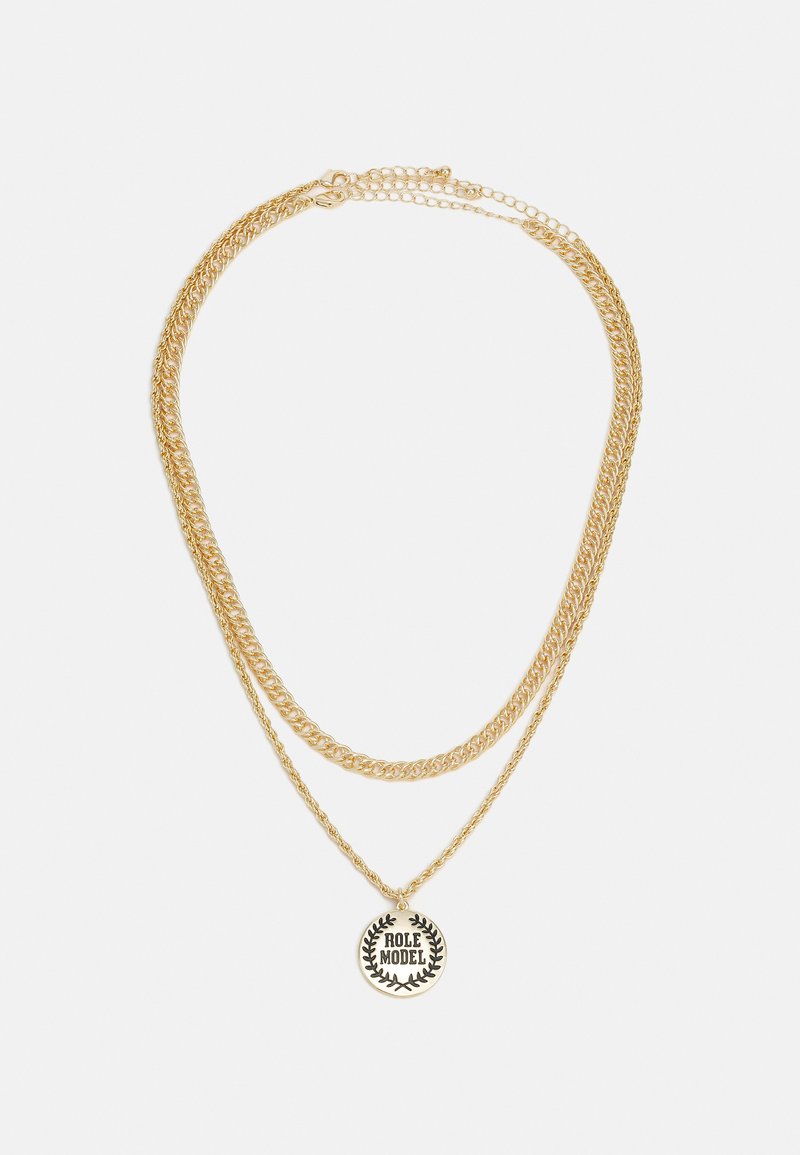 Colar em camadas douradas com duas correntes de espessuras variadas, com um pendente circular exibindo o texto "MODELO A SEGUIR" rodeado por um design de louro.