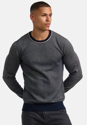Suéter de punto gris oscuro con un patrón texturizado, cuello redondo azul marino y puños y cintura de canalé en azul marino. Diseño ajustado con mangas largas.