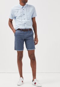 Ljusblå kortärmad skjorta med knappar och ficka, matchad med mörkblå shorts som är uppvikta i fållen och ett flätat brunt bälte. Vita sneakers.