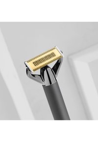 Guld- og sort hårtrimmer med en fintandet klinge, ergonomisk greb og elegante metalliske detaljer, designet til præcisionspleje.