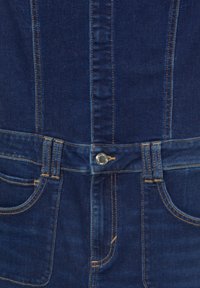 Ciemnoniebieski dżins z widocznymi szwami, z zapięciem na guziki i przednimi kieszeniami. Gładka tekstura, dopasowany krój.