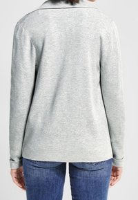 Šedá polokošile s dlouhým rukávem a límečkem, vyrobená z měkké tkaniny. Disponuje úzkým rib e a lemem, navržena s jemnou texturou.