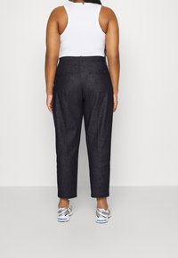 Donkerdenim broek met een hoge taille, rechte pijpen en achterzakken. Gestyled met een witte tanktop en grijze sportschoenen.