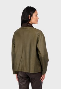 Oliwkowa skórzana kurtka z ciemnobrązowym kołnierzem z kordurowego materiału, luźny krój i widoczne detale szwów, zestawiona z brązowymi skórzanymi spodniami.