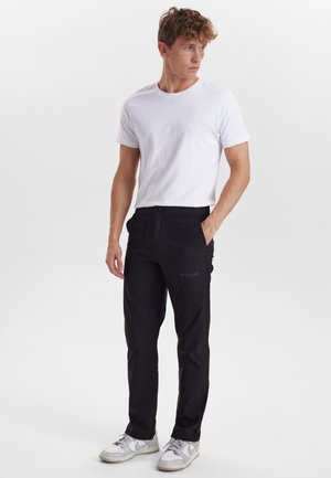 Sorte, tapered bukser med en glat tekstur, der har en forkantlomme og subtil branding. Parret med en tætsiddende hvid t-shirt med rund hals og sneakers.