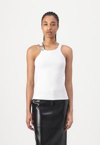 Witte geribde mouwloze top met een zilveren hardware accent op de schouder, gecombineerd met een zwarte leren rok, die een getailleerd silhouet laat zien.