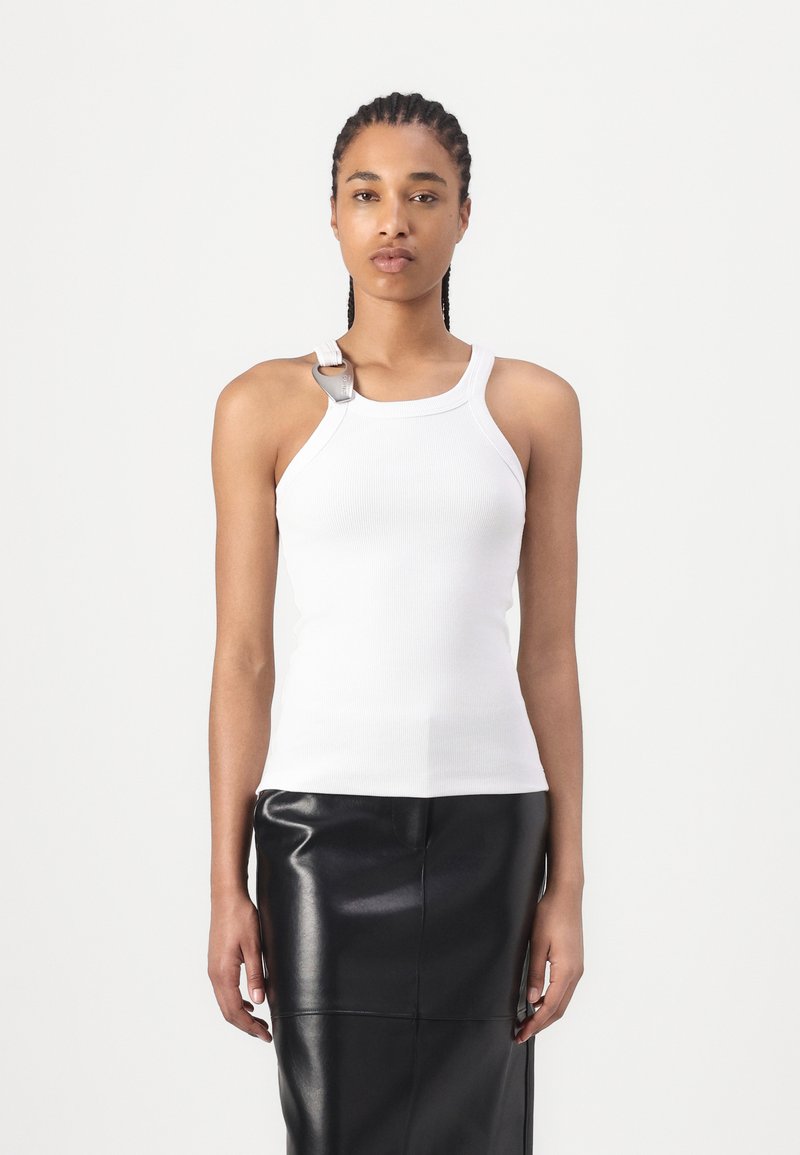 Witte geribde mouwloze top met een zilveren hardware accent op de schouder, gecombineerd met een zwarte leren rok, die een getailleerd silhouet laat zien.