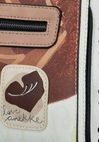 Bolso multicolor con una textura estampada que presenta un prominente parche en forma de corazón etiquetado "love anekke" y una cremallera negra.